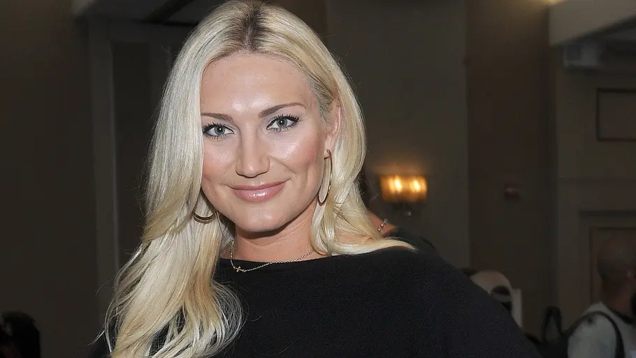 Brooke Hogan in schwarzem Outfit posiert lächelnd bei einer Veranstaltung in einem Innenraum.
