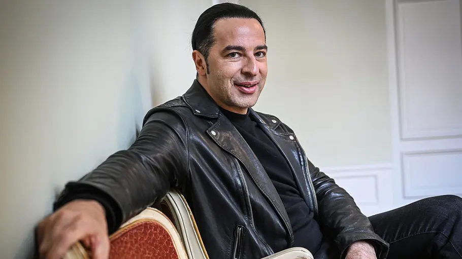 Bülent Ceylan Bülent Ceylan sitzt lächelnd auf einem Stuhl, sein Arm ist über die Lehne eines anderen Stuhl gelehnt.