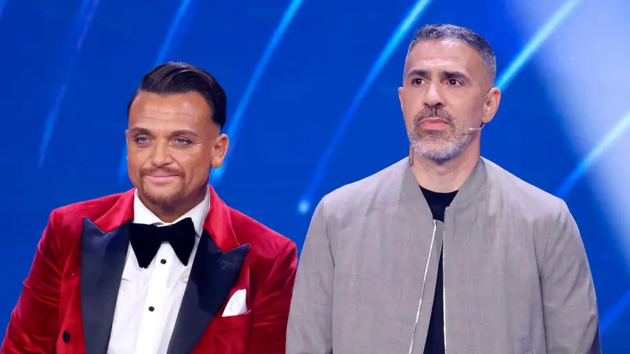 Menowin Fröhlich und Bushido Menowin trägt ein rotes Sakko und steht lächelnd neben einem ernsten Bushido.
