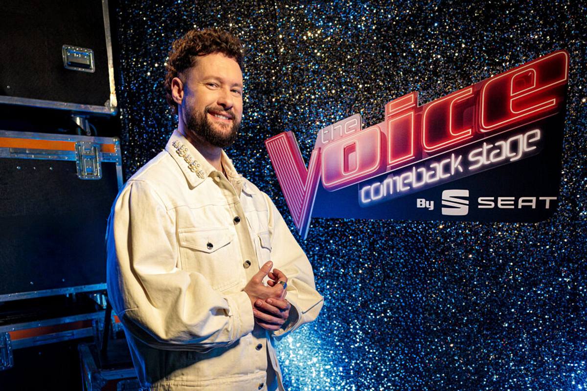 Der Sänger Calum Scott mit braunen Locken trägt ein weißes Hemd und posiert vor dem Logo der Show.