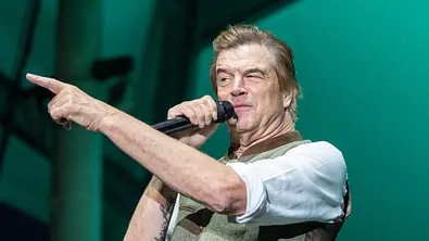 Tote Hosen-Frontsänger Campino steht auf einer Bühne, hält ein Mikrofon in der rechten Hand und zeigt mit ausgestrecktem linken Arm zur Seite. - Foto: IMAGO / Funke Foto Services
