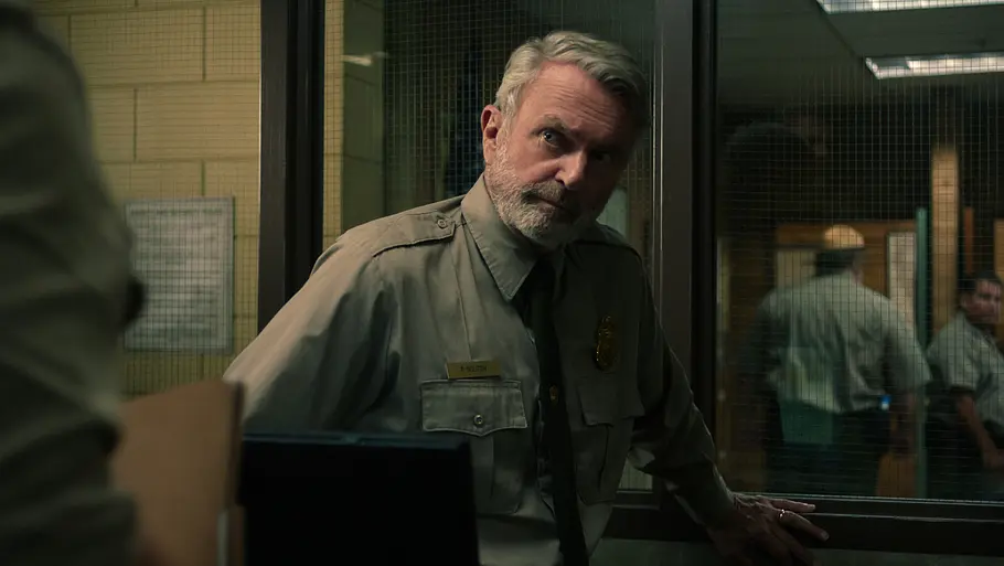 Sam Neill als Paul Souter. Er schaut fragend die Person vor sich an, sein halbes Gesicht liegt im Schatten.