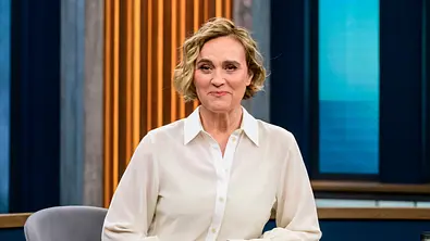 Caren Miosga sitzt in einem weißen Hemd an einem Talkshow-Tisch.  - Foto:  IMAGO / HMB-Media