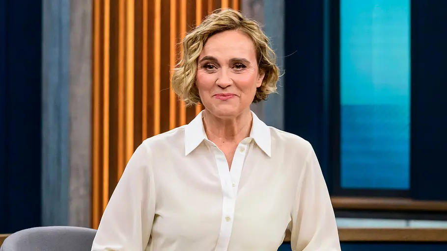 Caren Miosga Caren Miosga sitzt in einem weißen Hemd an einem Talkshow-Tisch.