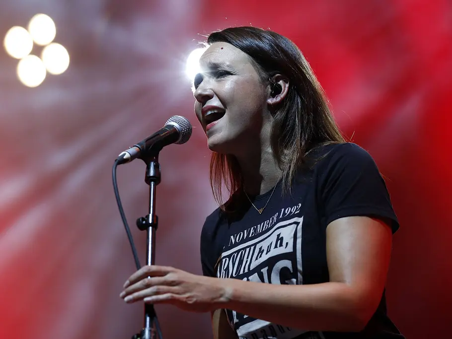 Carolin Kebekus bei der „Helene Fischer Show“ 2026 Carolin Kebekus steht im schwarzen T-Shirt an einem Mikrofon vor rotem Bühnenlicht und weißen Scheinwerfern.