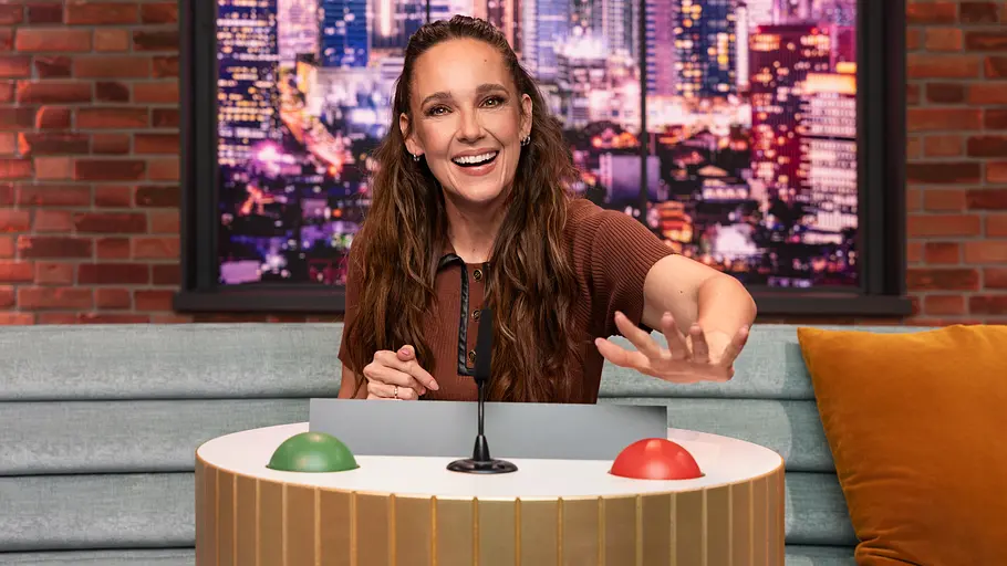 Carolin Kebekus ist zwar ein alter „LOL“-Hase, ab jetzt ist lachen für sie aber erlaubt. Carolin Kebekus lacht hinter einem Pult mit Mikrofon sowie grünem und rotem Knopf und streckt eine Hand nach vorn.