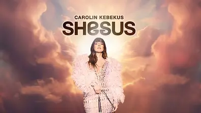 Promotional poster mit der Aufschrift „Carolin Kebekus SHESUS“: Eine Frau im rosafarbenen, federbesetzten Outfit steht mit Mikrofon vor einem himmlischen Hintergrund aus Wolken und goldenem Licht. - Foto: WDR/Marvin Ruppert