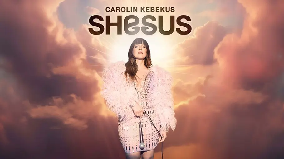 Caroline Kebekus Shesus Promotional poster mit der Aufschrift „Carolin Kebekus SHESUS“: Eine Frau im rosafarbenen, federbesetzten Outfit steht mit Mikrofon vor einem himmlischen Hintergrund aus Wolken und goldenem Licht.