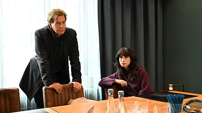 Caspar Bergmann (Thomas Heinze) steht hinter einem Stuhl in einem Konferenzzimmer. Annabell Lorenz (Stephanie Stumph) sitzt neben ihm am Tisch. Vor den beiden auf dem Tisch stehen Gläser und Wasserflaschen. - Foto:  ZDF/Barbara Bauriedl