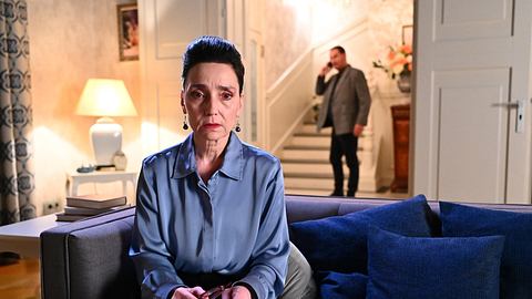 Simone sitzt auf der Couch in ihrer Villa und schaut traurig in Richtung Kamera, im Hintergrund telefoniert Richard und schaut in ihre Richtung bei Alles was zählt - Foto: RTL / Julia Feldhagen