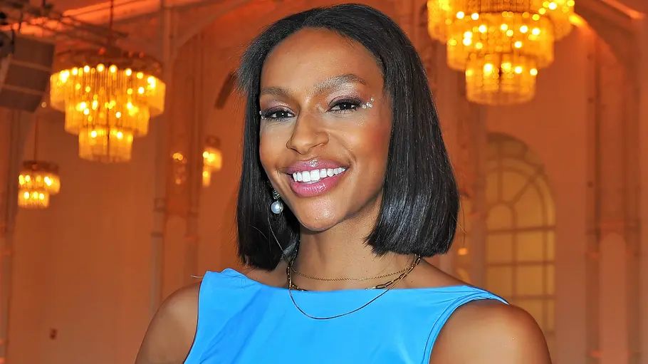 Cecilia Asoro: Eine lächelnde Frau mit schwarzem Bob trägt ein blaues Kleid in einem Saal mit Stuhlreihen und leuchtenden Kronleuchtern.