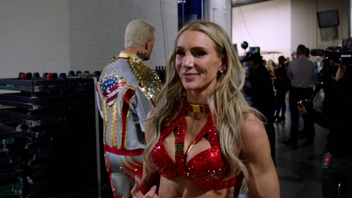 Charlotte Flair ist die Tochter von WWE-Legende Ric Flair. Charlotte Flair gibt ein Interview, hinter ihr geht Cody Rhodes vorbei.