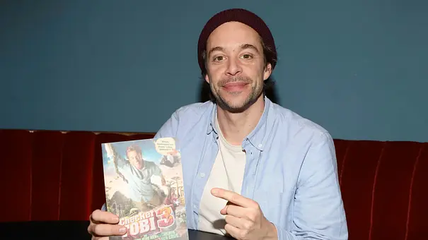 Tobias Krell zeigt auf das Poster zum Film: „Checker Tobi 3 und lächelt in die Kamera. - Foto: IMAGO / Future Image Tobias Krell zeigt auf das Poster zum Film: „Checker Tobi 3 und lächelt in die Kamera. - Foto: IMAGO / Future Image