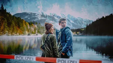 Schnee von Gestern - Landkrimi: Chefinspektorin Melanie Grandits (Marlene Hauser) und Chefinspektor Martin Steiner (Simon Morzé) stehen am Ufer. Im Vordergrund verläft ein Absperrband der Polizei, im Hintergrund liegt ein Bergpanorama. - Foto: ZDF / Landsiedl /Stefanie Leo.