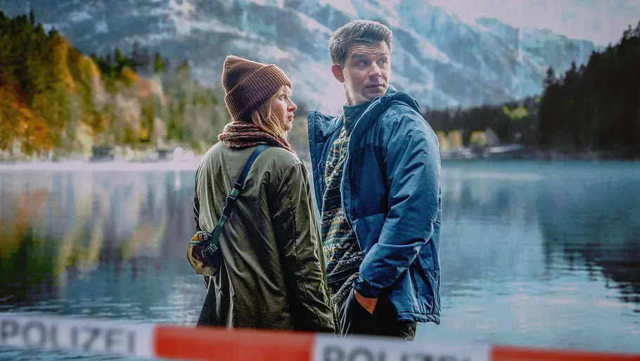 Chefinspektorin Melanie Grandits (Marlene Hauser) und Chefinspektor Martin Steiner (Simon Morzé) ermitteln. Schnee von Gestern - Landkrimi: Chefinspektorin Melanie Grandits (Marlene Hauser) und Chefinspektor Martin Steiner (Simon Morzé) stehen am Ufer. Im Vordergrund verläft ein Absperrband der Polizei, im Hintergrund liegt ein Bergpanorama.