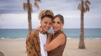 Chika und Carina stehen eng umschlungen vor einem Strand mit Palmen und Meer und schauen in die Kamera. - Foto: RTL / Jonas Mohr Chika und Carina stehen eng umschlungen vor einem Strand mit Palmen und Meer und schauen in die Kamera. - Foto: RTL / Jonas Mohr