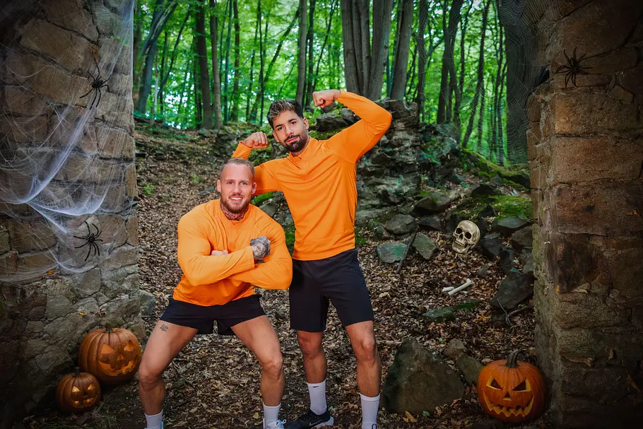 Chris Kugathasan & Jerry Chris Kugathasan & Jerry posieren zwischen Steinmauern mit Spinnweben, Kürbissen und einem Schädel im Wald.