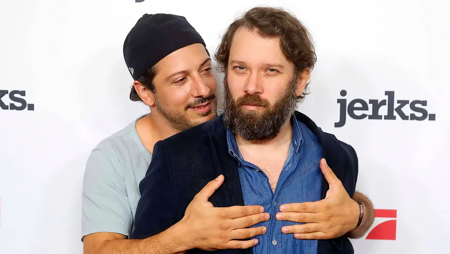 Christian Ulmen – Jerks Christian Ulmen steht mit Fahri Yardim vor einer Fotowand für „jerks.“. Yardim umarmt ihn von hinten.