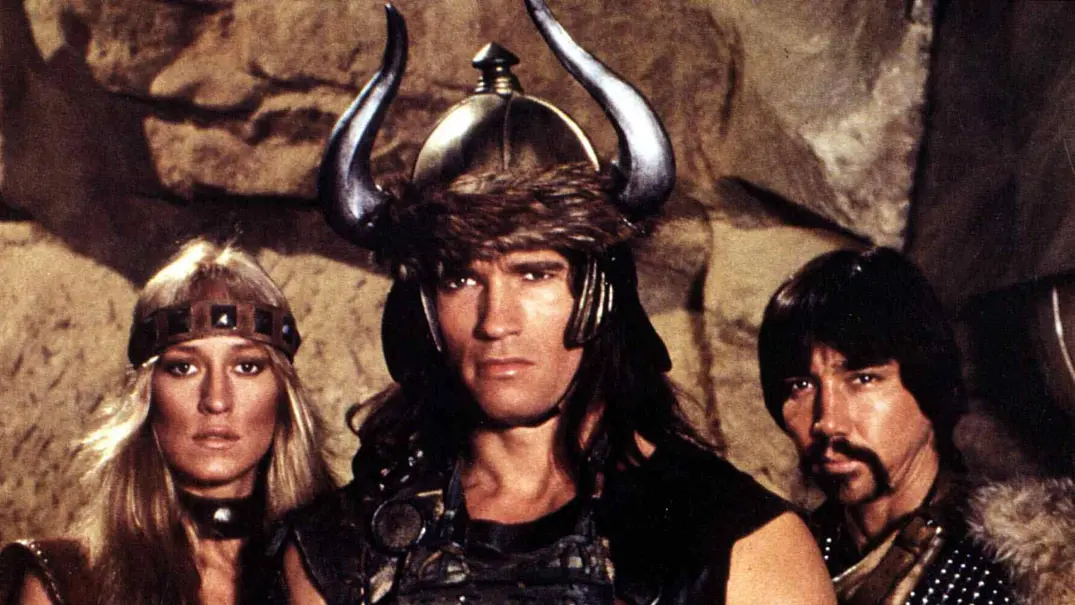 Arnold Schwarzenegger steht in Barbaren-Montur neben zwei weiteren Personen in derselben Montur. - Foto:  IMAGO / United Archives