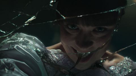 Eine junge Frau im weißen Hochzeitskleid blickt mit bedrohlichem Lächeln durch einen zerbrochenen Spiegel. Es handelt sich um Mia Tomlinson als Judy Warren in „Conjuring 4: Das letzte Kapitel“. - Foto: © 2025 Warner Bros. Entertainment Inc. 
