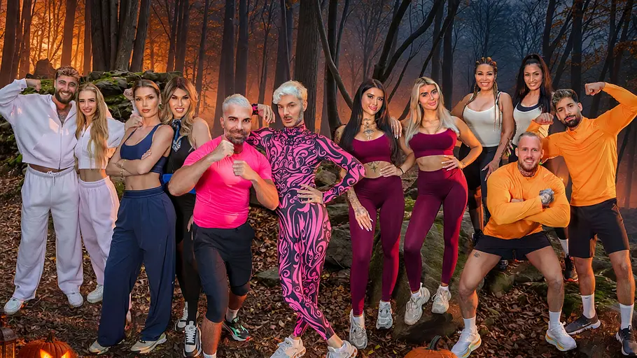 Couple Challenge Elf Kandidaten von #CoupleChallenge in bunter Sportkleidung posieren vor einer düsteren Waldkulisse mit Fledermäusen und leuchtenden Kürbissen.