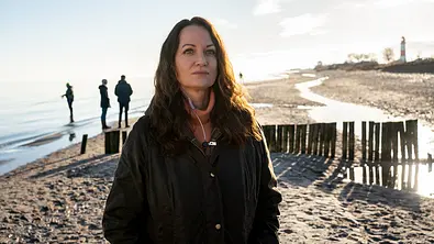 Ermittlerin Jana Winter steht in Wintermontur an einem Strand.  - Foto: ZDF/Georges Pauly