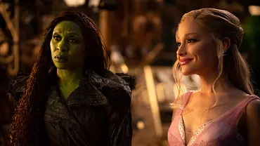 Cynthia Erivo als Elphaba schaut skeptisch. Sie hat grüne Haut und trägt ein schwarzes Gewand. Ariana Grande als Glinda lächelt freundlich, strahlt und trägt ein rosa Kleid. - Foto: Universal Studios Cynthia Erivo als Elphaba schaut skeptisch. Sie hat grüne Haut und trägt ein schwarzes Gewand. Ariana Grande als Glinda lächelt freundlich, strahlt und trägt ein rosa Kleid. - Foto: Universal Studios