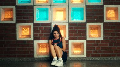 Hauptdarstellerin Mila sitzt vor einer Wand mit verschiedenen farbigen Leucht-Kacheln.  - Foto: RTL / Zeitsprung