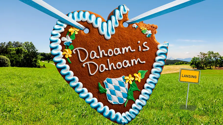 Dahoam is Dahoam Man sieht das Logo von „Dahoam is Dahoam“ vor einer grünen Wiese, auf der ein Ortsschild des Ortes Lansing steht.