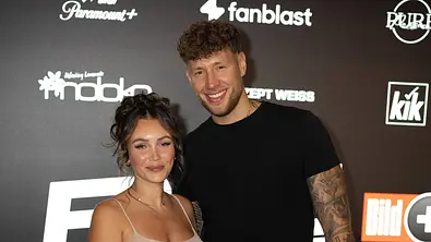 Dana Feist im langen, beigen Glitzerkleid und Wilson Coenen in Schwarz posieren auf einem roten Teppich vor einer Logowand. - Foto: IMAGO / BOBO Dana Feist im langen, beigen Glitzerkleid und Wilson Coenen in Schwarz posieren auf einem roten Teppich vor einer Logowand. - Foto: IMAGO / BOBO