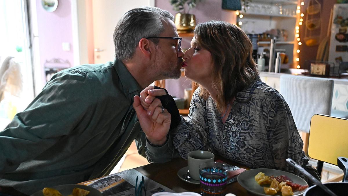 Daniela und Henning küssen sich am Essenstisch.