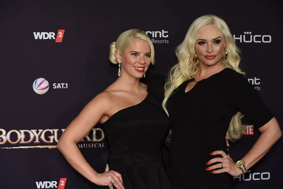 Daniela Katzenberger und Jenny Frankhauser Daniela Katzenberger und Jenny Frankhauser posieren in schwarzen Kleidern vor einer dunklen Wand mit Sponsorenlogos.