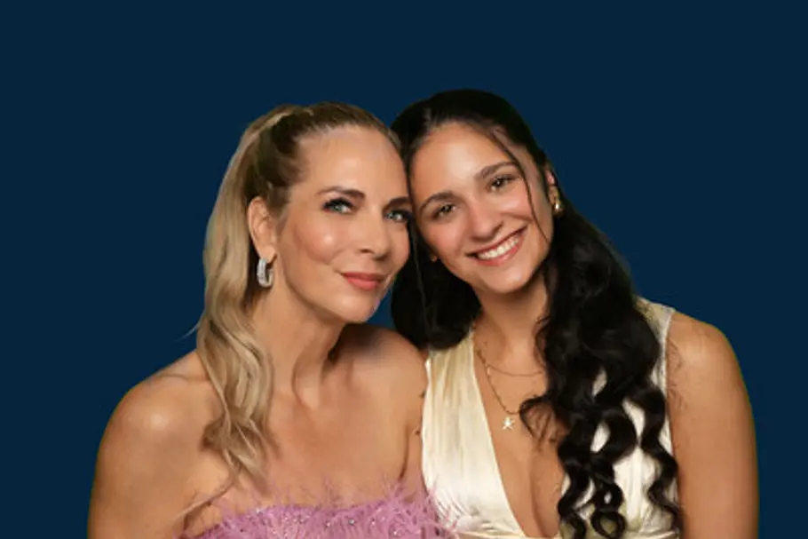 Danni Büchner im rosa Kleid und Tochter Jada Karabas im cremefarbenen Kleid posieren lächelnd vor dunkelblauem Hintergrund.