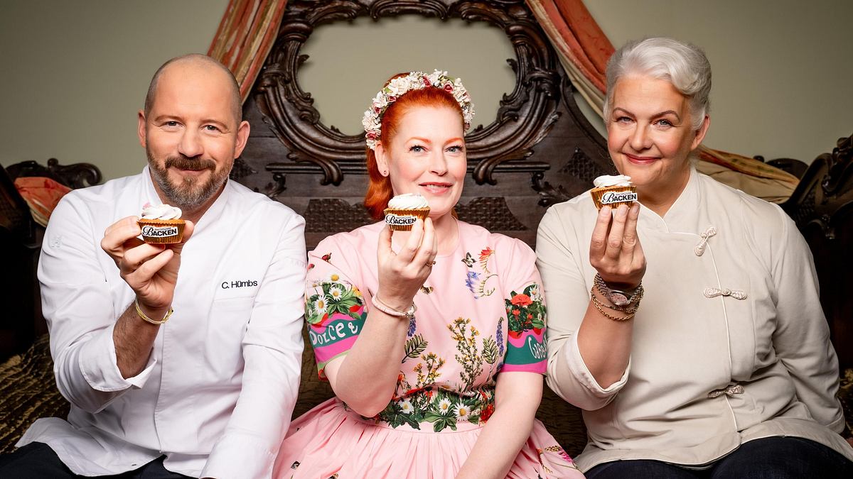 Die Jury von „Das große Backen“ posiert, alle drei halten einen Cupcake in der Hand