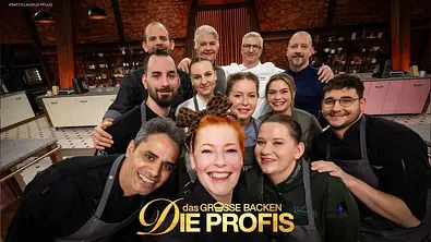 Gruppen-Selfie von zwölf Personen in einer professionellen Backstube. Die Teilnehmenden tragen Kochjacken und Schürzen und lächeln gemeinsam in die Kamera. Im Hintergrund sind Arbeitsflächen, Regale und Küchengeräte zu sehen. Über dem Bild ist das Logo der TV-Show „Das große Backen – Die Profis“ eingeblendet. - Foto: Joyn / Claudius Pflug Gruppen-Selfie von zwölf Personen in einer professionellen Backstube. Die Teilnehmenden tragen Kochjacken und Schürzen und lächeln gemeinsam in die Kamera. Im Hintergrund sind Arbeitsflächen, Regale und Küchengeräte zu sehen. Über dem Bild ist das Logo der TV-Show „Das große Backen – Die Profis“ eingeblendet. - Foto: Joyn / Claudius Pflug
