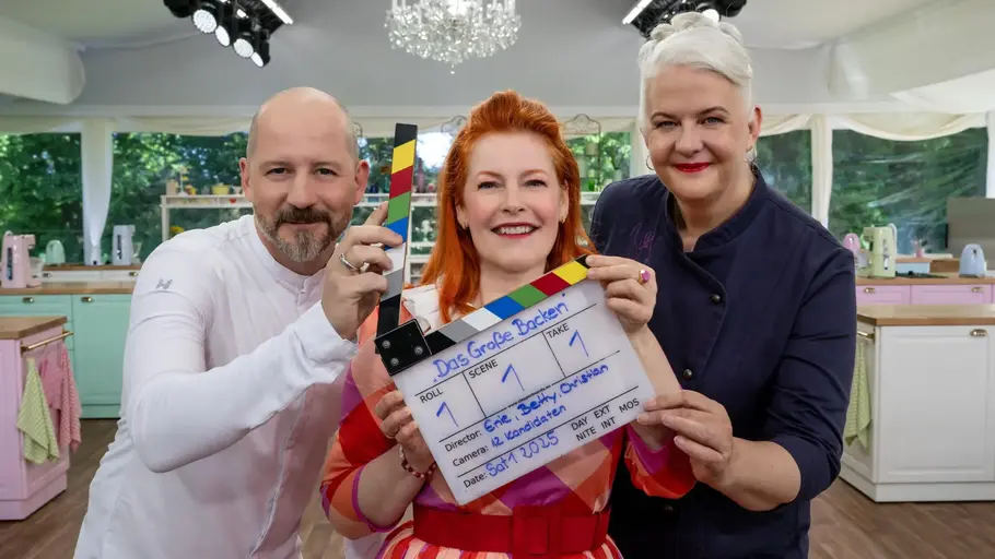„Das große Backen – Die Profis“: Jury und Moderatorin im Backzelt Christian Hümbs, Enie van de Meiklokjes und Bettina Schliephake-Burchardt stehen im Backzelt von „Das große Backen – Die Profis“ und halten eine Filmklappe.