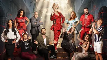 Gruppenbild eines Reality-TV-Casts vor einer dramatischen Kulisse: In einem beschädigten Gebäude mit eingestürzter Decke steht eine Person in einem auffälligen roten Outfit zentral auf einer Treppe und wird von Lichtstrahlen von oben beleuchtet. Um sie herum posieren mehrere weitere Personen in unterschiedlich auffälligen Outfits, einige mit betenden oder überraschten Gesten. Die Szenerie wirkt theatralisch und apokalyptisch, mit Rissen in den Wänden und rot glühenden Effekten im Hintergrund. - Foto: Joyn/Nikolai Milatovic Gruppenbild eines Reality-TV-Casts vor einer dramatischen Kulisse: In einem beschädigten Gebäude mit eingestürzter Decke steht eine Person in einem auffälligen roten Outfit zentral auf einer Treppe und wird von Lichtstrahlen von oben beleuchtet. Um sie herum posieren mehrere weitere Personen in unterschiedlich auffälligen Outfits, einige mit betenden oder überraschten Gesten. Die Szenerie wirkt theatralisch und apokalyptisch, mit Rissen in den Wänden und rot glühenden Effekten im Hintergrund. - Foto: Joyn/Nikolai Milatovic