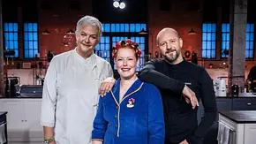 Betty, Enie und Christian in der TV-Show „Promibacken“ – die Jury steht gemeinsam in der Studioküche und lächelt in die Kamera. - Foto: SAT.1 / Claudius Pflug