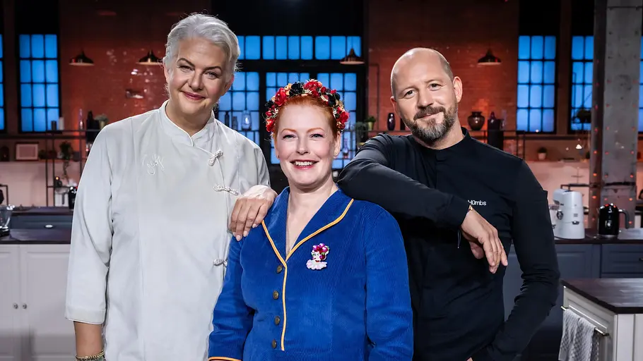 Promibacken Betty, Enie und Christian in der TV-Show „Promibacken“ – die Jury steht gemeinsam in der Studioküche und lächelt in die Kamera.