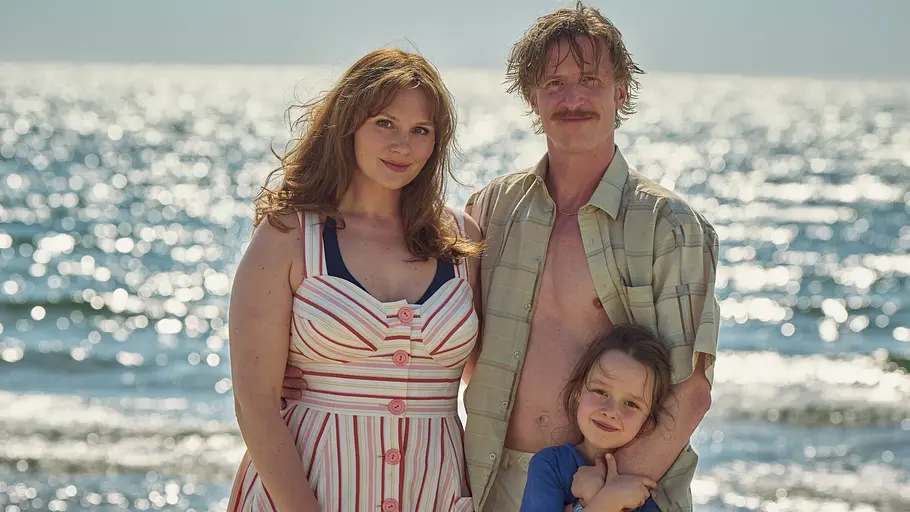 Das heile Familienleben existiert nur noch auf Fotos. Rosalie Thomass, Golo Euler und Elise Lindner stehen eng beieinander vor dem glitzernden Meer und schauen in die Kamera.