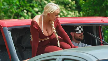 Michelle sitzt in roter Kleidung in der offenen Front eines roten Autos. Neben ihr trägt Sandro eine karierte Augenmaske. - Foto: RTL