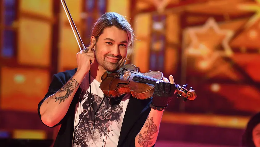 David Garrett ZDF Weihnachtsshow David Garrett hält eine Geige unter dem Kinn und einen Bogen in der Hand auf einer warm beleuchteten Bühne mit Sternendekor.