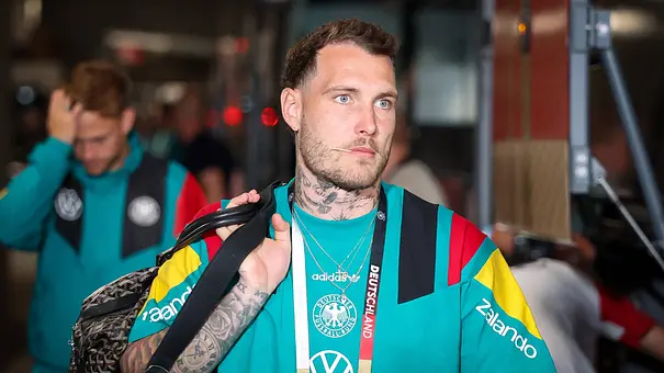 David Raum geht lässig mit einer Sporttasche einen Gang entlang. - Foto: IMAGO / kolbert-press