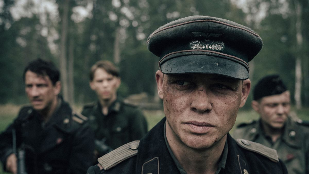 Im Vordergrund steht Leutnant Philip Gerkens (David Schütter) mit Schirmmütze und verschmutztem Gesicht, sein Blick ernst und angespannt. Hinter ihm sind seine Kameraden zu sehen: Christian (Laurence Rupp), Helmut (Leonard Kunz).