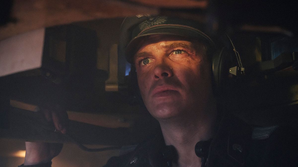 David Schütter in „Der Tiger“: Er sitzt im Panzer und blickt aus der Luke hinaus. Ein Auge zusammengekniffen, das andere wachsam. Auf dem Kopf trägt er große Kopfhörer und einen Helm, gekleidet in eine Wehrmachtsuniform des Zweiten Weltkriegs. 