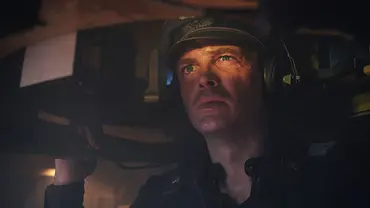 David Schütter in „Der Tiger“: Er sitzt im Panzer und blickt aus der Luke hinaus. Ein Auge zusammengekniffen, das andere wachsam. Auf dem Kopf trägt er große Kopfhörer und einen Helm, gekleidet in eine Wehrmachtsuniform des Zweiten Weltkriegs.  - Foto: Amazon MGM Studios