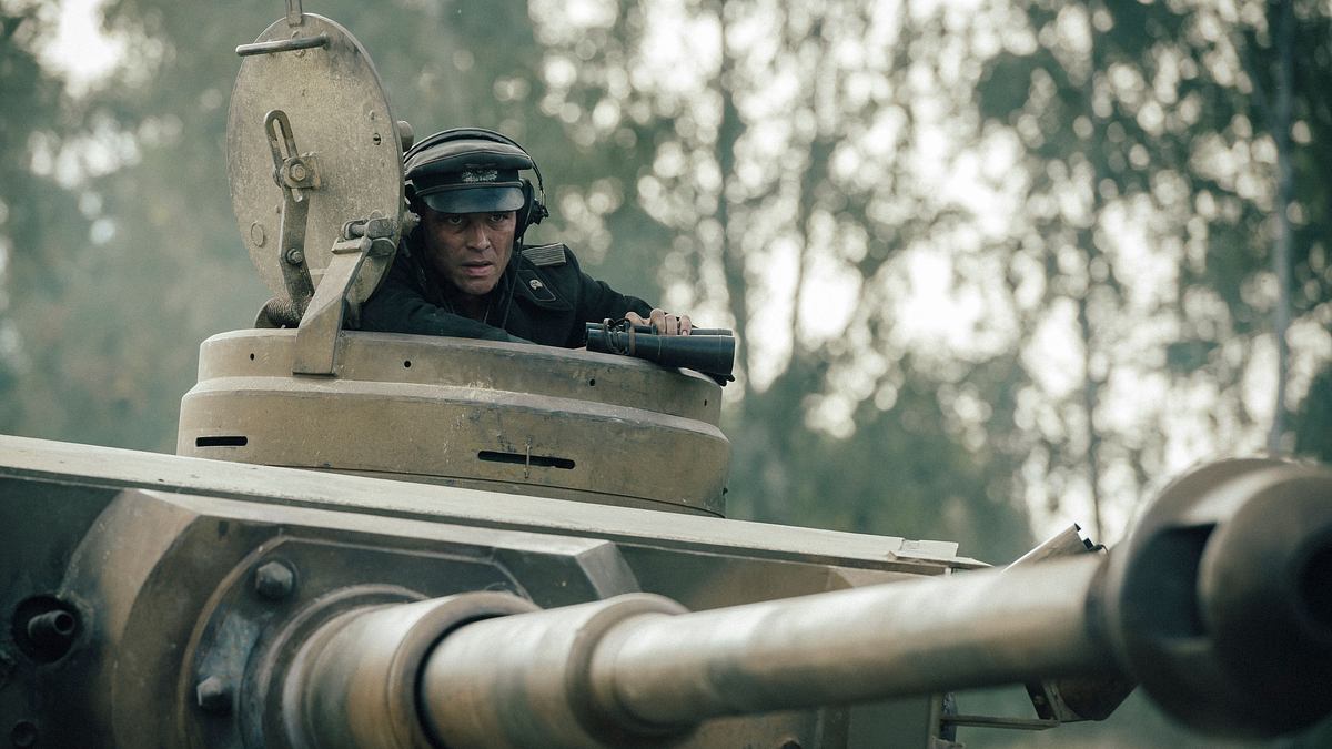 David Schütter in „Der Tiger“ als Leutnant Philip Gerkens: Er sitzt in seinem Panzer und schaut aus der Luke heraus. In der Hand ein Fernglas, der Blick konzentriert nach vorne gerichtet.