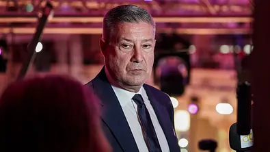 Joachim Llambi trägt einen dunklen Anzug mit Krawatte vor einer violett beleuchteten Kulisse. Rechts ist ein Mikrofon zu sehen. - Foto: Imago/STEINSIEK.CH