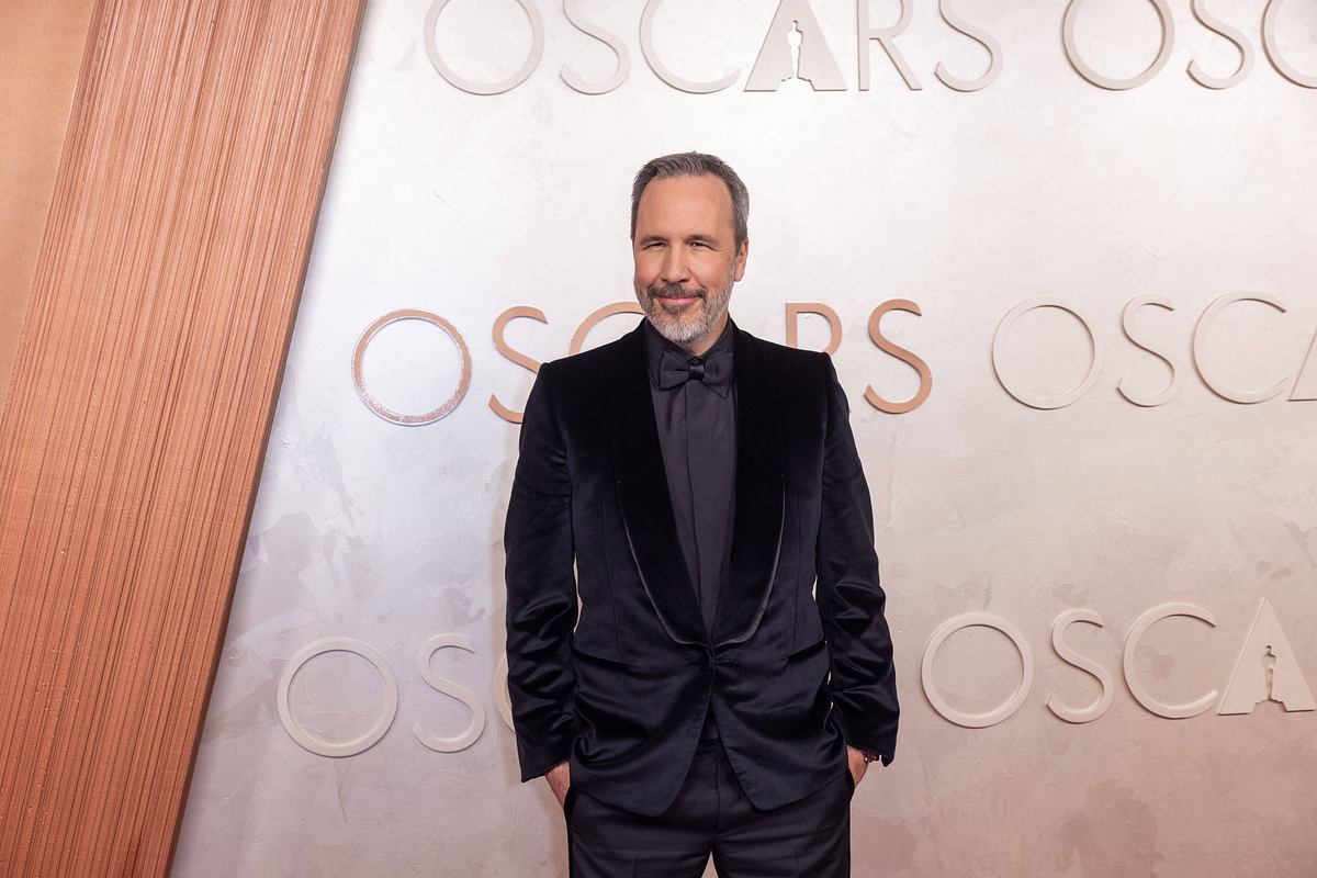 Denis Villeneuve Man sieht Regisseur Denis Villeneuve in einem schwarzen Anzug vor einer Fotowand der Oscars.