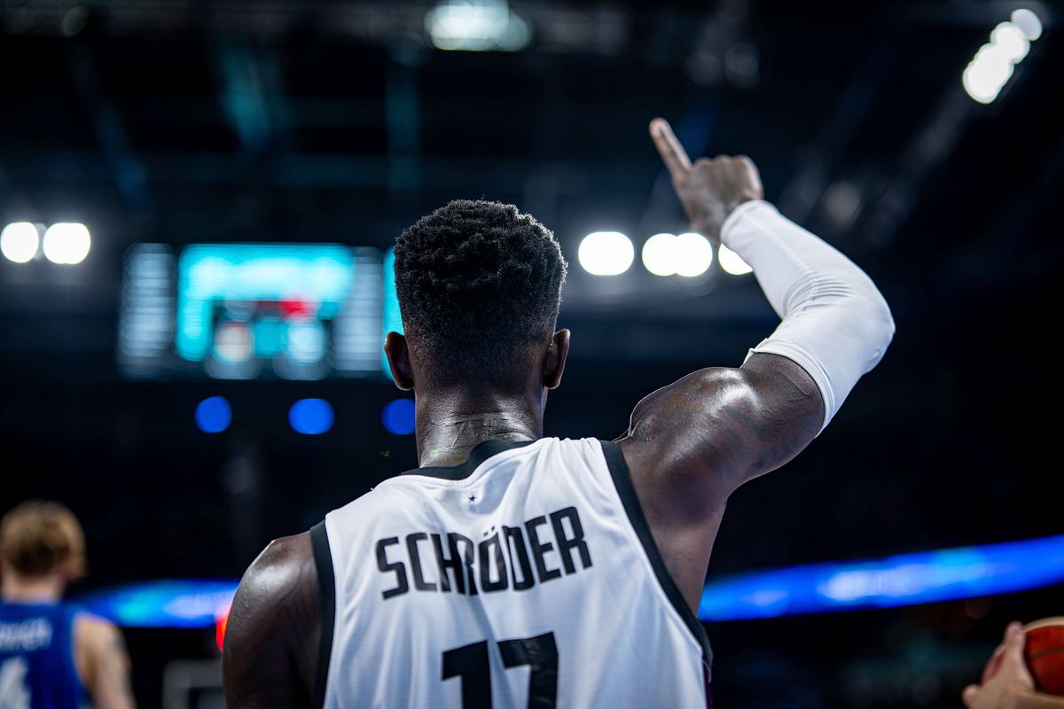 Dennis Schröder Deutschland Dennis Schröder ist mit dem Rücken zur Kamera. Man sieht sein Basketball-Trikot. Er zeigt mit dem rechten Zeigefinger nach oben.